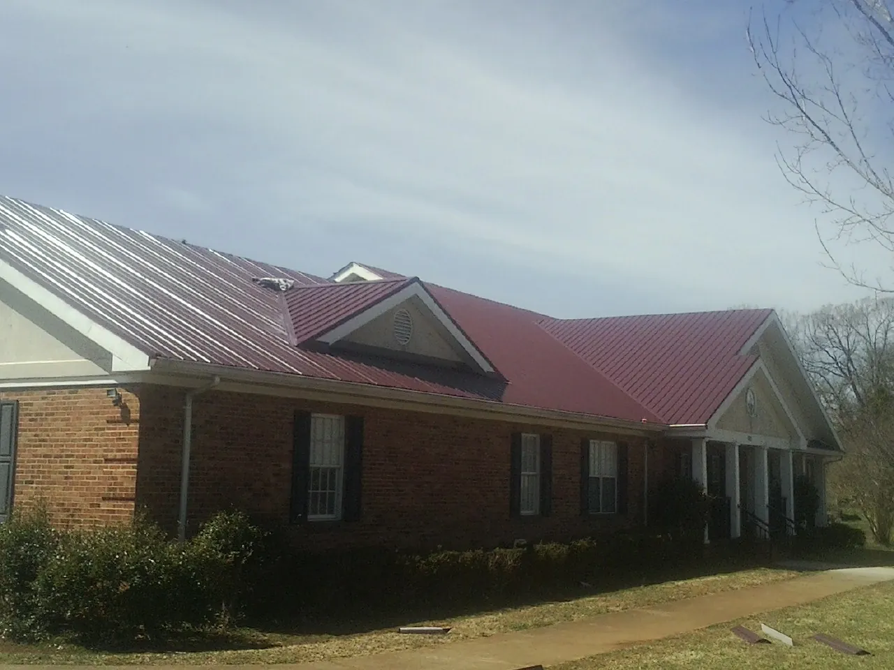Red metal roof with gabled entries on a long brick building, from a Hail Damage Roof Repair job in Oberlin