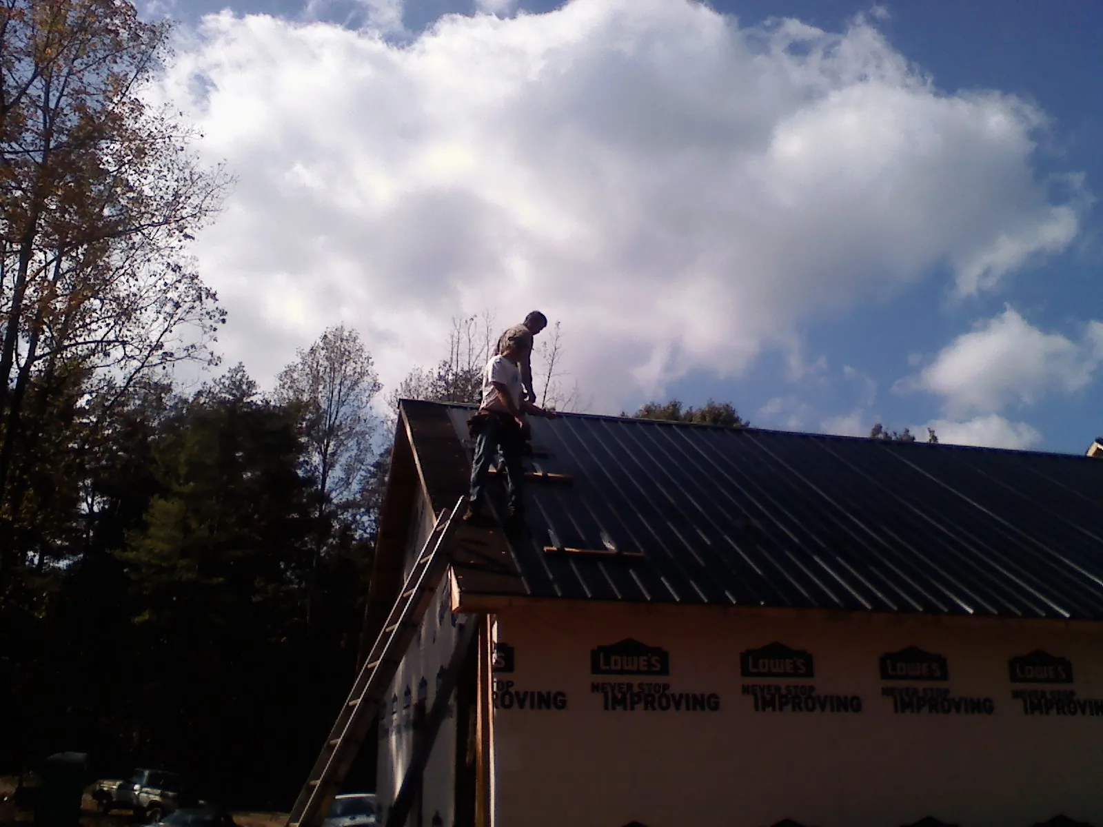 Roofer fastening dark metal panels high against a cloudy sky, from a Roof Inspection job in Oberlin
