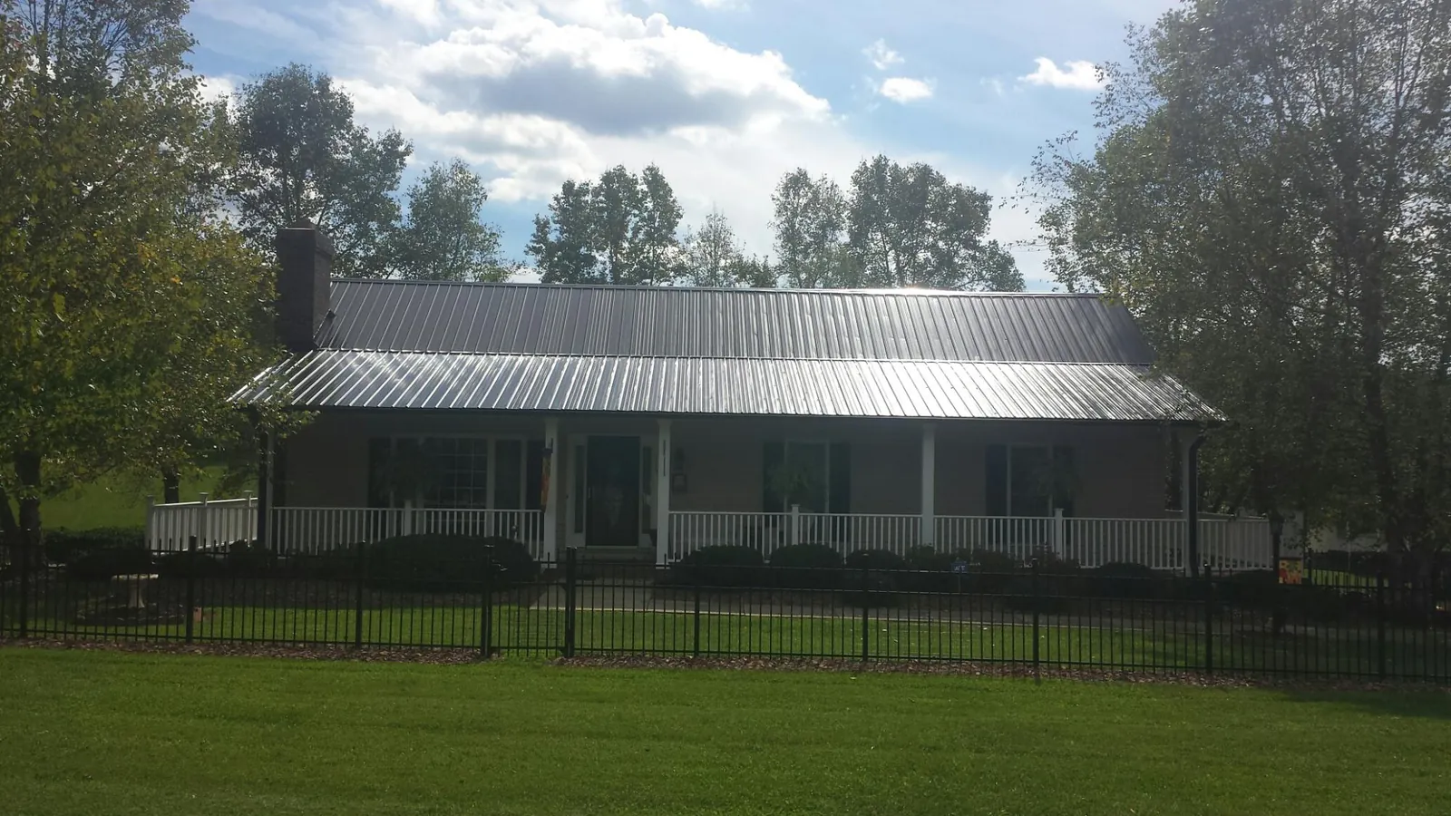Gray metal roof on a brick ranch with a full width front porch — Gutter Guard Installation work by our crew in Oberlin