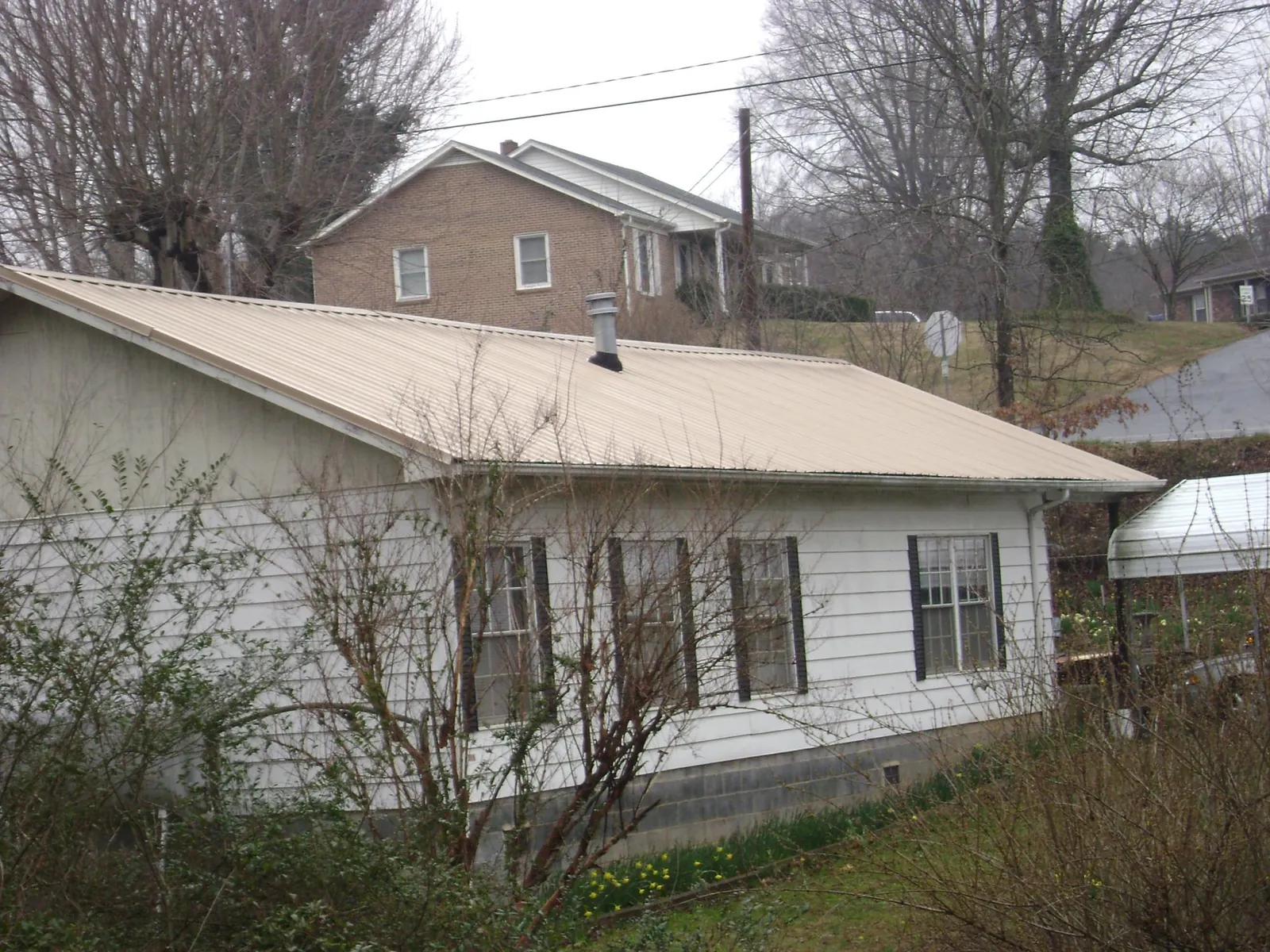 Tan metal roof on a white sided house set into a hillside — Commercial Roofing by Roofing Brothers in Oberlin