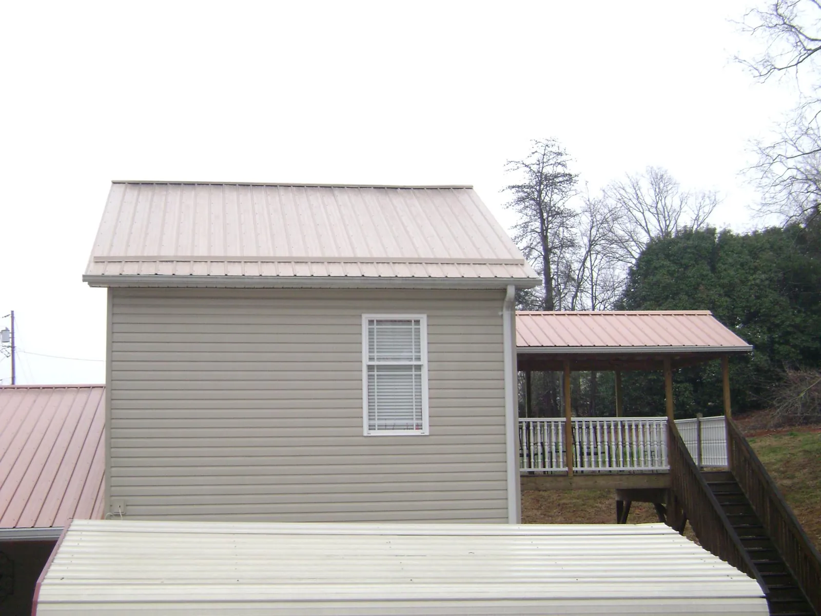 Tan metal roofs on a two story addition and attached porch, from a Roof Replacement job in Oberlin
